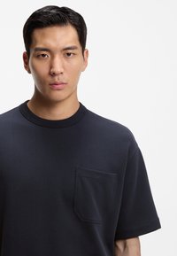 Marineblaues Baumwoll-T-Shirt mit rundem Ausschnitt und Brusttasche. Kurze Ärmel und glatte Textur, mit lockerem Schnitt.