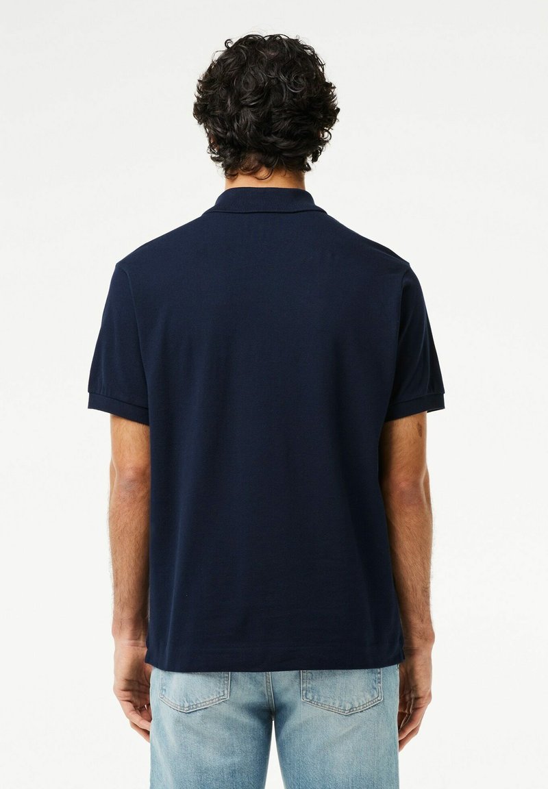 Polo shirt bleu marine à manches courtes, col rabattu, avec une texture lisse et une coupe décontractée, porté avec un jean bleu clair.