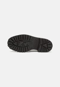 Semelle de botte noire avec des crampons profonds et robustes incluant des motifs triangulaires et linéaires pour une meilleure traction sur fond blanc plat.