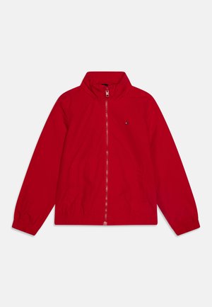 Chaqueta cortavientos roja con cierre frontal, cuello alto, puños elásticos y dos bolsillos laterales. Presenta un pequeño logotipo en el lado izquierdo del pecho.