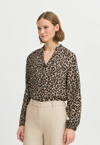 Leopardenmuster Bluse aus leichtem Stoff mit V-Ausschnitt und langen, leicht gerafften Ärmeln, kombiniert mit beigen, hochtaillierten Hosen.
