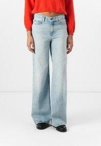 Lyseblå høytaljede vidjeans med en falmet vask, kontrasterende sømmer og fem-lommers design, kombinert med en kort rød genser.
