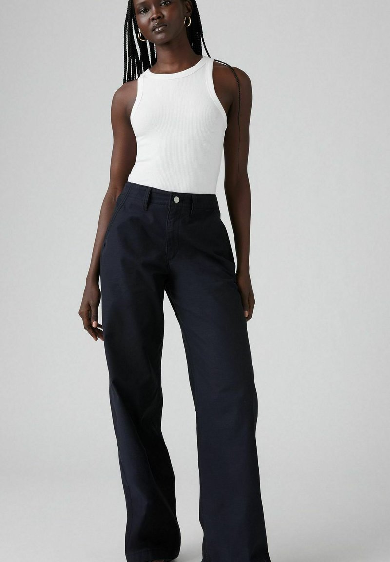 Top bianco a coste abbinato a pantaloni larghi blu navy con tasche frontali e chiusura a bottone, texture liscia e vestibilità sartoriale.