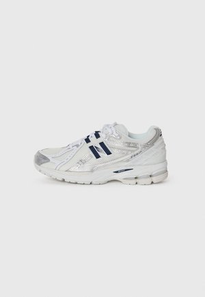 Scarpa sportiva argento e bianca con tomaia in rete, suola in gomma e dettagli in blu navy. Presenta una punta arrotondata e un tallone imbottito per supporto.