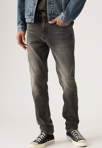 Γκρι τζιν από τζιν ύφασμα με ξεθωριασμένο φινίρισμα, ίσιο κόψιμο στα πόδια, εμπρόσθιες τσέπες και θηλιές για ζώνη, συνδυασμένα με μαύρα mid-top αθλητικά παπούτσια.