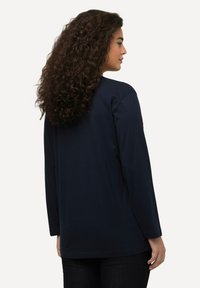 Marineblaues Langarmshirt mit Rundhalsausschnitt, lockerer Passform und weichem Baumwollstoff. Dezente Nähte und ein abgerundeter Saum am unteren Ende.