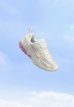 Chaussure de sport Nike blanche et rose flottant sur un fond de ciel bleu clair.