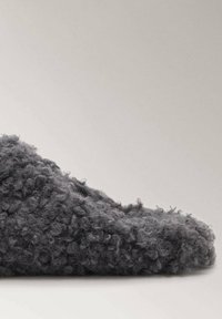 Fuzzy grijze slipper met een zachte, gestructureerde oppervlakte en ronde vorm, met een casual, instapontwerp voor comfort.