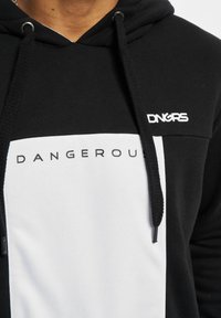 Felpa nera e bianca con una sezione superiore testurizzata nera e un pannello inferiore bianco liscio. Presenta il testo "DANGEROUS" e i lacci del cappuccio.