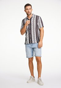 Camisa de manga corta en blanco y negro con patrones geométricos, combinada con pantalones cortos de mezclilla desgastados en azul claro y zapatillas grises.