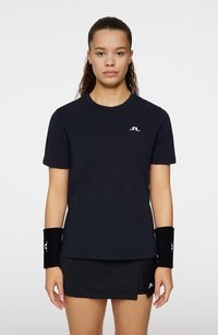 Svart idrottströja med korta ärmar och rund halsringning, prydd med en vit logotyp på bröstet; matchas med en svart kjol och handledsskydd.