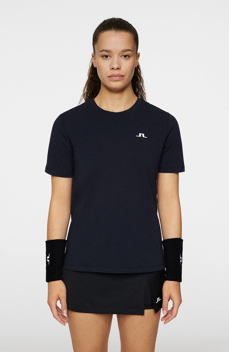 Svart idrottströja med korta ärmar och rund halsringning, prydd med en vit logotyp på bröstet; matchas med en svart kjol och handledsskydd.