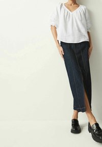 Weiße, strukturierte Bluse mit V-Ausschnitt und Puffärmeln, kombiniert mit einem langen, dunklen Jeansrock mit einem Schlitz vorne und kontrastierenden Nähten.