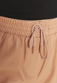 Hellerosa, glatte Jogginghosen mit elastischem Bund, Kordelzug, Seitentasche und gerafftem Textil entlang der Taille.