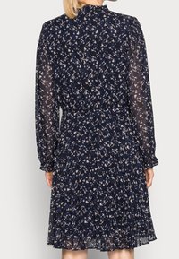 Mörkblå klänning med långa genomskinliga ärmar, samlad midja och veckad kjol. Har ett blommönster i ljusa färger på en mörk bakgrund.