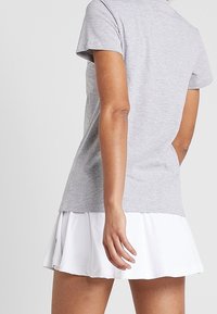 Szary top z krótkim rękawem i okrągłym dekoltem, zestawiony z białą warstwową spódnicą, ukazujący gładką fakturę i sportowy design.