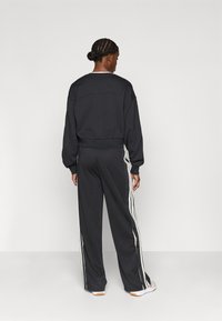 Čierna mikina s dlhými rukávmi a rebrovanými manžetami, doplnená čiernymi teplákmi s bielymi bočnými pruhmi a gombíkovými detailmi.