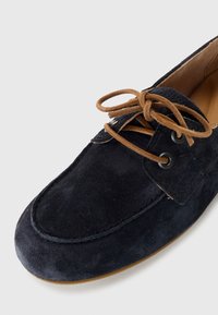 Navy blue suede shoe with a rounded toe, brown laces, metal eyelets, and a stitched design along the upper. Flat tan rubber sole.