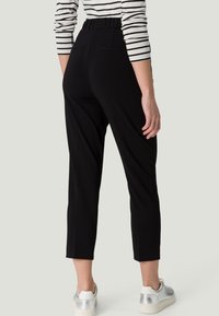 Pantalon noir à texture douce, taille élastique et longueur cropped. Le dos présente deux poches et une finition lisse. Associé à des baskets.