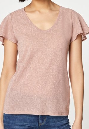 Lichtroze top met korte mouwen en V-hals, subtiele glans, zachte textuur en gerimpelde mouwen. Gecombineerd met spijkerbroek.