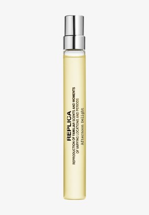 Flacon de parfum en verre transparent et fin avec un bouchon argenté, liquide jaune clair à l'intérieur, étiqueté parfum Replica Afternoon Delight.