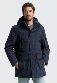 Námornícka parka s kapucňou, zipsom a patentkami, viacerými vreckami a textúrovaným povrchom. Navrhnutá pre teplo a ochranu.