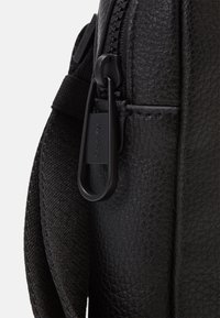 Borsa nera in pelle texturizzata, con una zip liscia e un attacco a clip nera. Include una tracolla in tessuto per il trasporto.