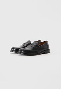 Black leather loafers with a rounded toe, front straps, and a flat heel. Smooth texture with minimal accents and a classic design.