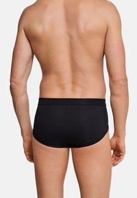 Slip da bagno neri con un design a coste testurizzate e cintura elastica, visti da dietro, che mettono in mostra una silhouette aderente.