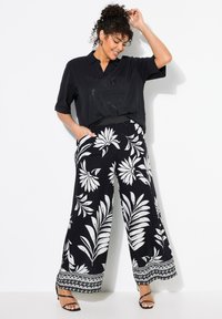 Černé tričko s krátkým rukávem a grafickým designem, spárované s širokými kalhotami se bílým květinovým vzorem a vzorovaným lemem.