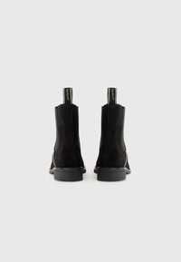 Bottes de cheville en suède noir avec une finition lisse, dotées d'un petit talon carré et de tirants en boucle. Design simple sans embellissements visibles.