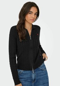 Czarny kardigan z dzianiny w splot warkoczowy z zapięciem na zamek i kołnierzem; posiada mały czerwony wzór serca na klatce piersiowej; ściągacze przy mankietach i u dołu.