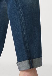 Donkerblauwe denim jeans met opgerolde manchetten, met een soepele textuur en contrasterende lichtgekleurde draden langs de naden.