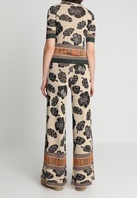 Conjunto de dos piezas que incluye un top ajustado y pantalones de pierna ancha. Confeccionado en tela beige con estampados de hojas y flores negras. Detallado con una cinturilla naranja con la marca.