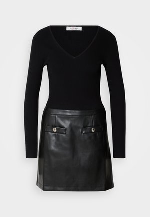 Svart ribbet langermet topp med V-hals, kombinert med et svart skinnminiskjørt med frontlommer og metallknapper.