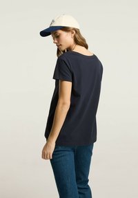 Granatowa bawełniana koszulka z okrągłym dekoltem, krótkimi rękawami i luźnym krojem, w połączeniu z dwukolorową czapką z białym przodem i niebieskim daszkiem.