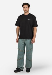Black short-sleeve t-shirt with logo, paired with light blue denim jeans featuring frayed seams and embroidered detailing, worn with black sneakers.