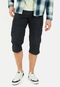 Black cargo shorts, knee-length, made of lightweight fabric, featuring multiple pockets and a relaxed fit, paired with white sneakers.