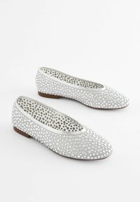 Paire de chaussures de ballet plates argentées avec des strass ronds et des semelles brunes, vues de côté sur fond blanc.