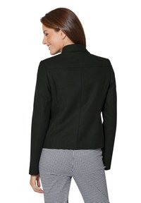 Zwarte tailleurjacket met een getailleerde pasvorm, geknipt kraag en textiele stof. Gestyled met zwart-wit geblokte broek.
