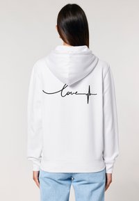 Felpa bianca con una grande scritta in corsivo nera "love" e un design di battito cardiaco sulla schiena. Presenta un cappuccio con cordino e polsini a costine.