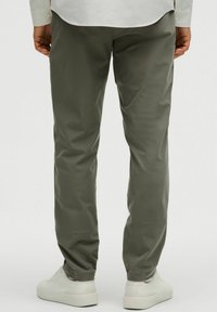 Szaro-zielone spodnie slim fit z gładkiego materiału, o minimalistycznym designie. Noszone z białymi sneakersami, tworząc czysty, nowoczesny wygląd.