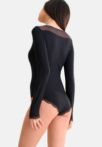 Bodysuit noir à manches longues présentant un empiècement en tulle à pois et une bordure en dentelle festonnée sur les bords, créant une silhouette ajustée et lisse.