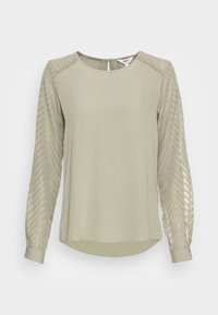 Blusa verde chiaro con maniche lunghe a chevron strutturate. Tessuto morbido, scollo rotondo, dettaglio a oblò sul retro e orlo leggermente curvato.