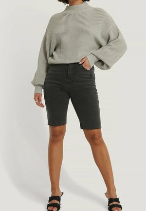 Personne portant un pull en maille gris clair ample avec des manches ballon, un short en jean noir jusqu'aux genoux, et des sandales noires tressées à bouts ouverts.