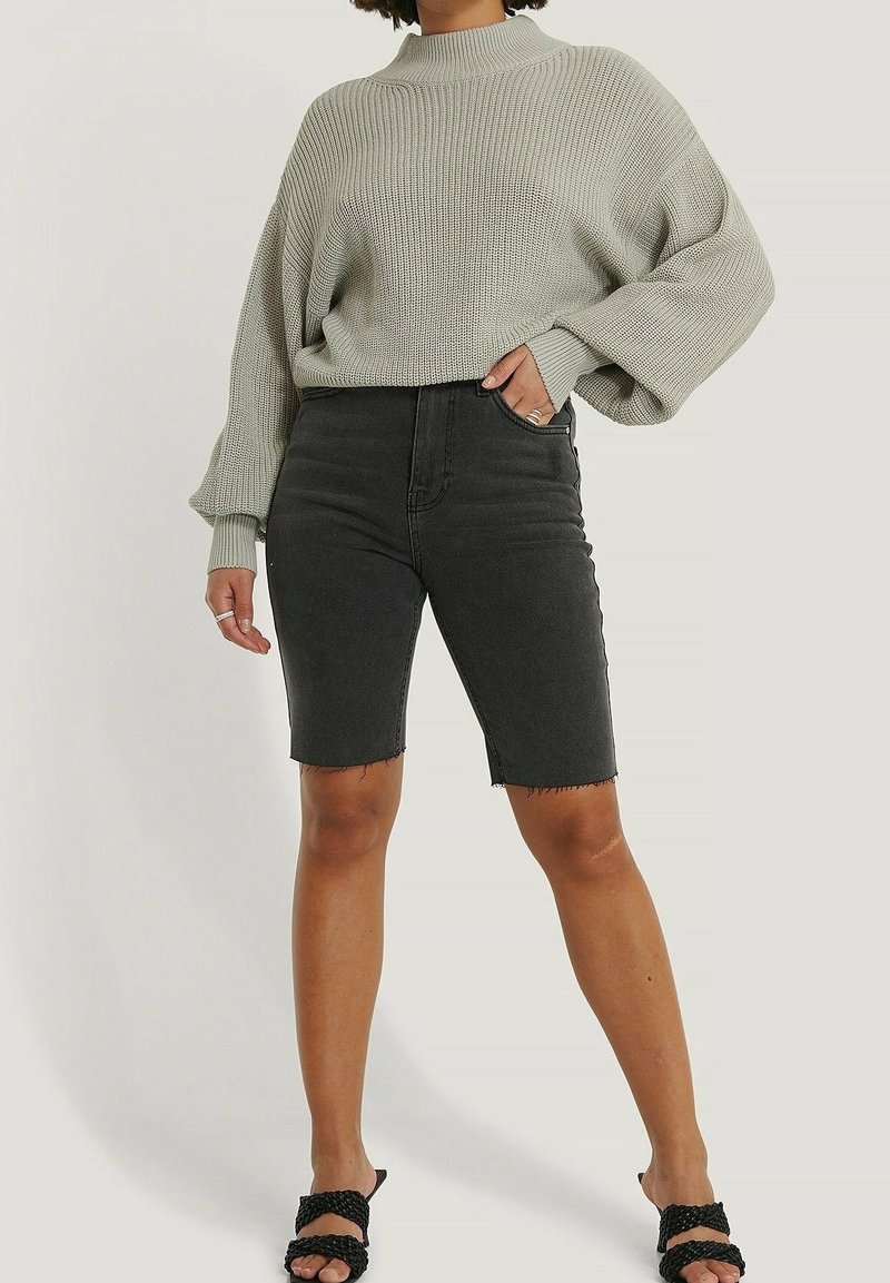 Personne portant un pull en maille gris clair ample avec des manches ballon, un short en jean noir jusqu'aux genoux, et des sandales noires tressées à bouts ouverts.