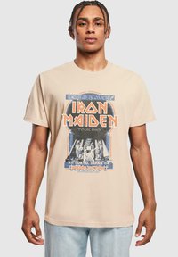 Tricou din bumbac bej, cu un print grafic al turneului Iron Maiden din 1985, cu accente albastre și portocalii și un design retro.