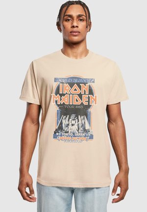 Beige Baumwoll-T-Shirt mit einem grafischen Druck der Iron Maiden-Tour von 1985, mit blauen und orangefarbenen Akzenten sowie einem retro Design.