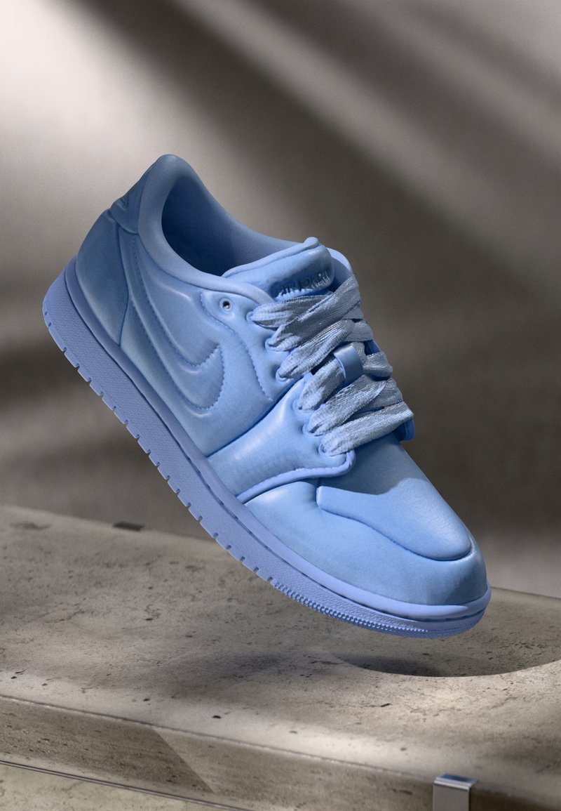 Šviesiai mėlyna Nike Air Jordan 1 sportbačių pora, su lygiu oda, paminkštintu liežuvėliu, pilkais raišteliais ir tekstūruota guma padanga. Paprasti dizaino akcentai.