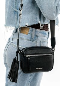 Black leather crossbody bag with a textured finish, zippered compartment, and tassel accents. Adjustable strap attached.
